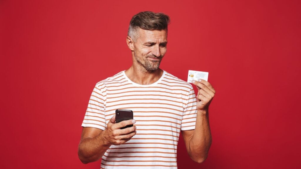 一个失望的男人拿着手机看着信用卡的肖像